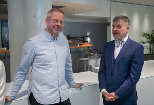 Kaksi henkilöä seisovat pöydän ääressä odottavan näköisinä.