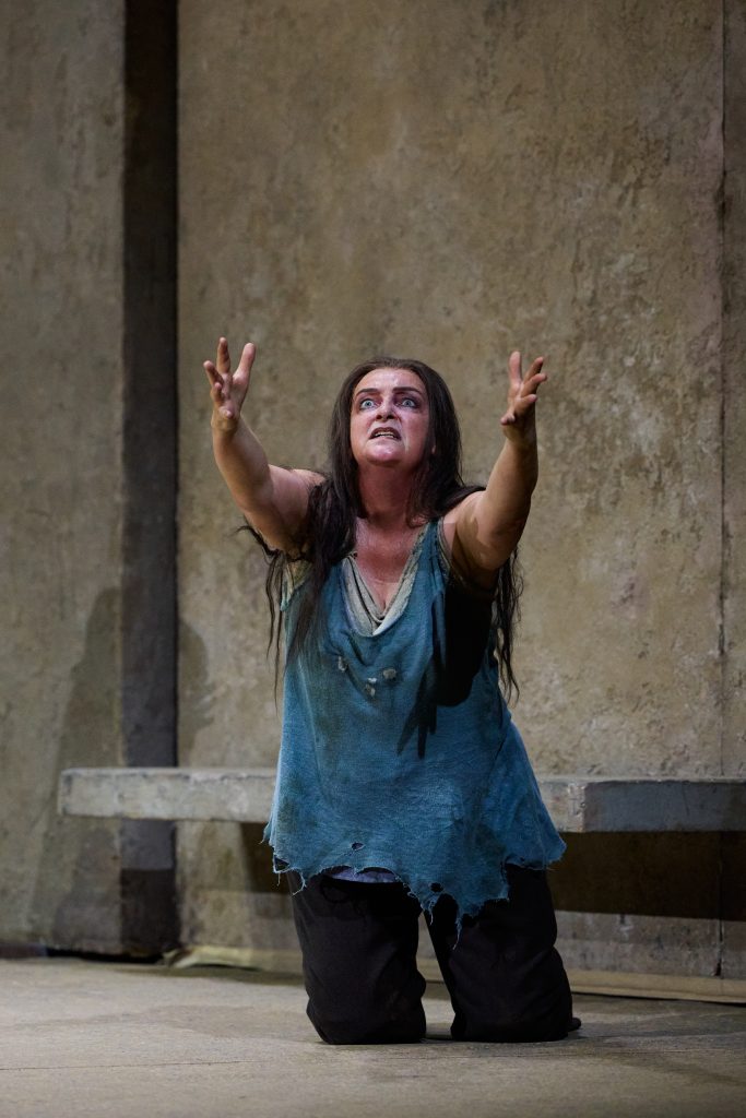 Nainen seisoo polvillaan ja kohottaa käsiään ylöspäin, kasvoillaan hypnotisoitunut ilme. Hänellä on päällään hihaton, sininen ja rikkinäinen paita sekä tummat housut. Hänen hiuksensa ovat pitkät, tummat ja kiharat. Tausta on vaalea.